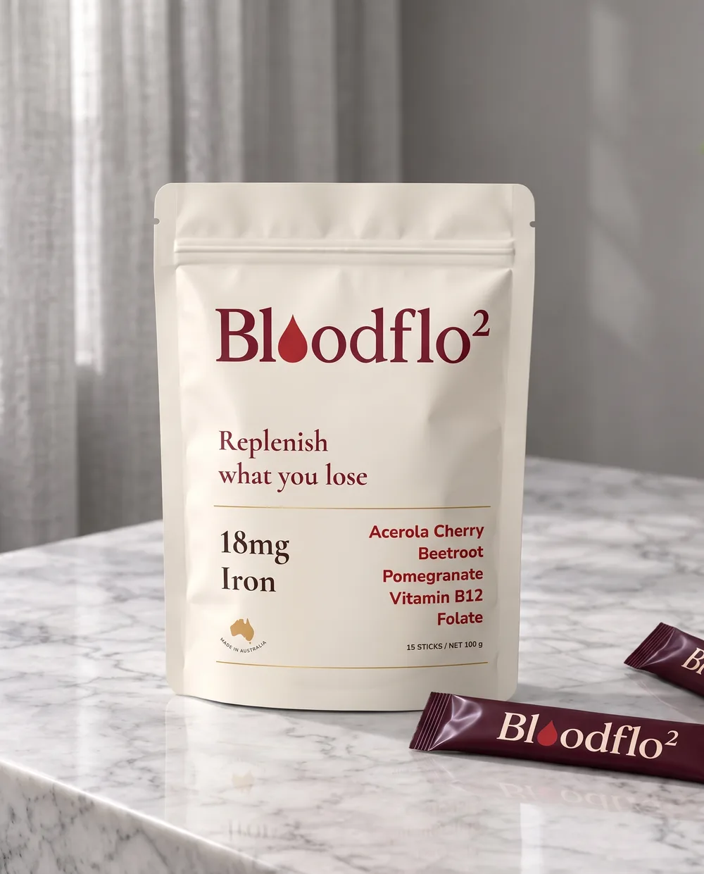 A cream Bloodflo Replenish bag standing on a kitchen bench with burgundy stick sachets beside it